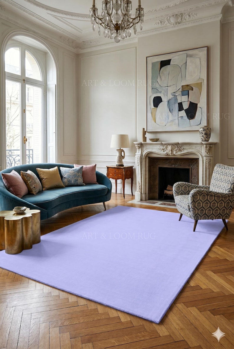 May include: A large, rectangular, solid lavender rug in a living room setting. The rug is the focal point, placed on a hardwood floor, with a teal sofa, patterned armchair, and abstract art in the background. The room has a classic, elegant style.