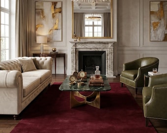 May include: A luxurious living room with a cream-colored sofa, green armchairs, and a dark red rug. A marble fireplace, gold-framed mirror, and a crystal chandelier add elegance. The room features abstract art and a coffee table with decorative items.