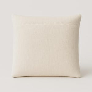 May include: A square, off-white pillow with a textured fabric. The pillow has a simple design with a stitched seam across the top. The neutral color and minimalist style make it suitable for various home decor themes.