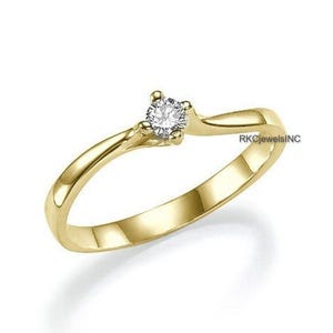 Puede incluir: Un anillo dorado con una sola gema redonda y transparente. El anillo tiene una banda lisa y pulida que se curva elegantemente hacia el engaste de la gema. Un diseño clásico, adecuado para diversas ocasiones.