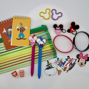 May include: A collection of Disney-themed stationery and accessories. Includes notebooks with Donald Duck and Goofy, pens with Mickey Mouse ears, stickers, a pencil case, keychains, and bracelets. The color palette is bright and playful.