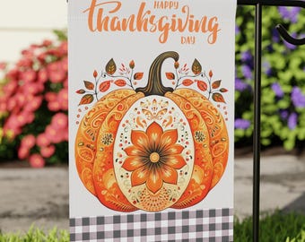 May include: A decorative garden flag featuring a detailed orange pumpkin design with floral accents and the words "Happy Thanksgiving Day" in orange script. The flag has a black and white checkered border and is displayed on a black metal stand.