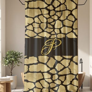 May include: A shower curtain with a gold and black pattern, featuring a dark band with a gold monogram. The curtain is hanging in a bathroom with a window, plants, and a wooden stool. The overall theme is bathroom decor.