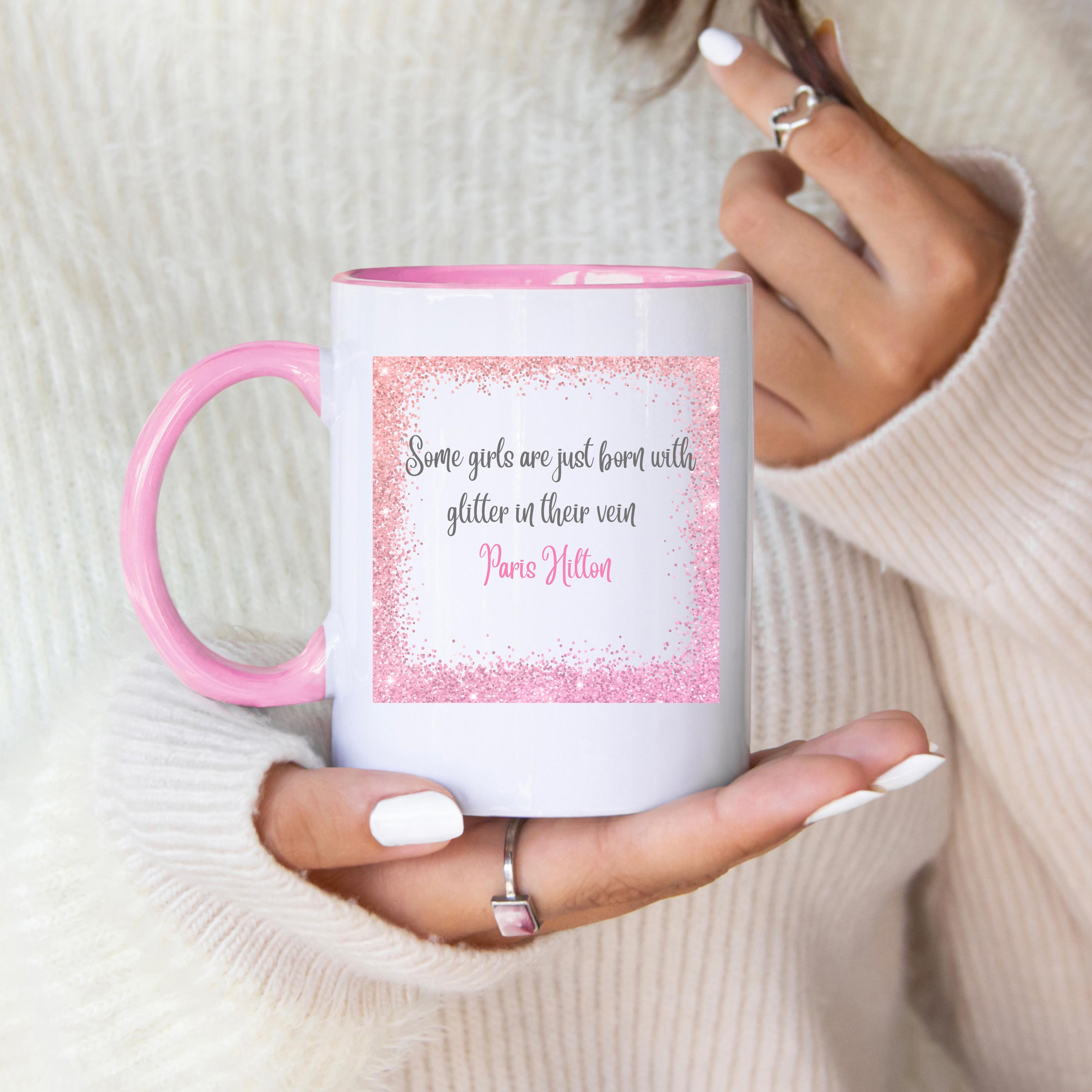 May include: White ceramic mug with a pink handle and interior. The mug features a pink glitter border around a quote that reads "Some girls are just born with glitter in their vein Paris Hilton."