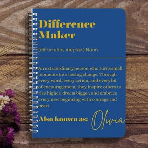 May include: A spiral-bound notebook with a blue cover featuring the words "Difference Maker" in yellow. The notebook includes a definition and inspirational text. The name "Olivia" is written in cursive at the bottom.
