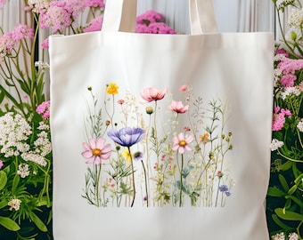 May include: Cream-colored tote bag featuring a watercolor floral design with pink, purple, and yellow flowers. The bag has sturdy handles and is set against a backdrop of pink and white flowers and a wooden surface.
