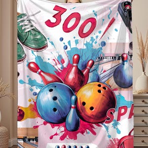 May include: White blanket with a colorful bowling-themed design. Features a large "300" in red, bowling pins, bowling balls, and a bowling shoe. The design includes splashes of blue, red, and pink.
