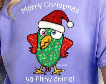 May include: Violet t-shirt featuring a Christmas parrot design. The parrot is adorned with a Santa hat and has a green body and red wings. The text on the shirt says "Merry Christmas ya filthy animal."