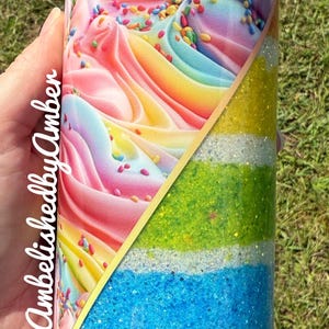 May include: A colorful tumbler with a diagonal design. The top half features a swirl of pink, yellow, and blue frosting with sprinkles. The bottom half is divided into glittery stripes of yellow, green, blue, silver, and purple.