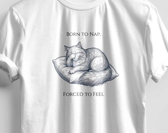May include: White t-shirt with a graphic of a sleeping cat on a pillow, with the text "BORN TO NAP, FORCED TO FEEL". The shirt is hanging on a black hanger. The brand name "TeeNest" is visible.