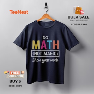 Può includere: T-shirt blu navy con la scritta colorata "DO MATH NOT MAGIC Show your work". La maglietta è appesa a una gruccia di legno su sfondo bianco. Il logo TeeNest è visibile in alto a sinistra.