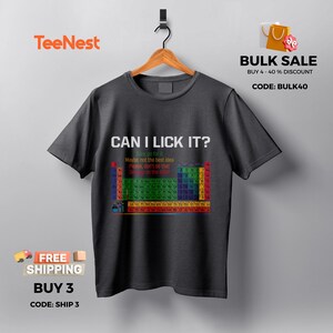 May include: Dark gray t-shirt with the text "CAN I LICK IT?" and a colorful periodic table design. The shirt also has the text "Maybe not the best idea, don't do that" and the TeeNest logo.