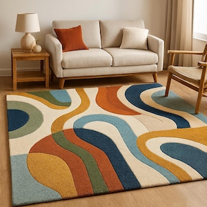 May include: A colorful area rug with a retro design. The rug features flowing, abstract shapes in shades of blue, orange, green, and yellow against a cream background. The rug is placed in a living room setting with a sofa, side table, and chair.
