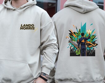 May include: Beige hoodie featuring the text "LANDO NORRIS" on the front. The back of the hoodie displays a colorful graphic of a person in a racing suit, with the number 4, celebrating near a race car.