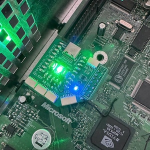 May include: Close-up of a green circuit board with a smaller green circuit board attached. The smaller board has the text "XB 12C EXP" and "RP2040-Zero". The Microsoft logo is visible. Several green and blue lights are illuminated.