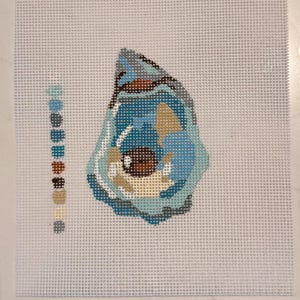 May include: Needlepoint canvas featuring a stylized oyster shell design. The shell is rendered in shades of blue, tan, and brown, with a detailed pattern. A color palette of coordinating hues is displayed to the left of the shell.