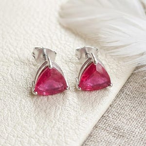 Peut inclure: Une paire de boucles d'oreilles à clous avec des pierres précieuses rouge rosé taillées en triangle à facettes, montées sur des griffes en métal argenté. Les boucles d'oreilles présentent un fermoir à poussette classique et une forme triangulaire.