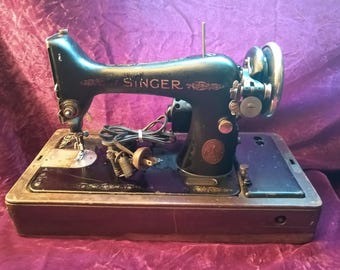 May include: Vintage Singer sewing machine, black with gold accents, on a wooden base. The Singer logo is prominently displayed. Features a hand wheel, needle, and various mechanical components. A classic sewing tool.