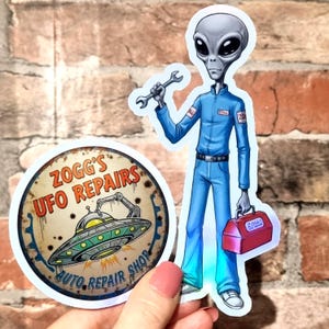 Pode incluir: Dois adesivos: um com um alienígena em macacão azul segurando uma chave inglesa e uma caixa de ferramentas, e outro com o texto "Zogg's UFO Repairs Auto Repair Shop" e um OVNI verde e prateado.