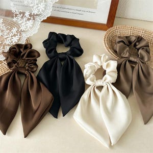 Può includere: Quattro elastici per capelli in tessuto con lunghi nastri pendenti. Il set include un elastico marrone scuro, uno nero, uno color crema e uno marrone chiaro. Ogni pezzo presenta una finitura liscia e satinata con centri elastici arricciati.
