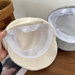 Op de afbeelding: Twee petten. E&eacute;n is beige, de andere grijs. Beide petten hebben een witte voering. De beige pet staat op de voorgrond en toont de binnenkant. De petten zijn gemaakt van een textuurstof.