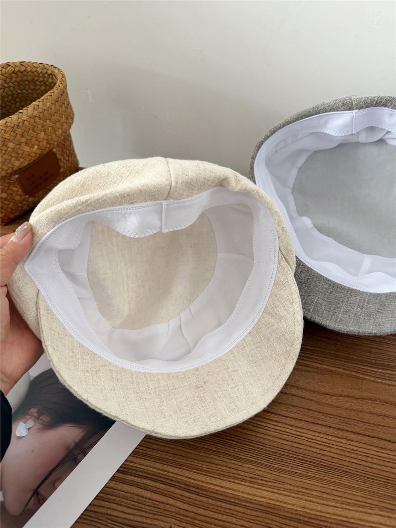 Op de afbeelding: Twee petten. E&eacute;n is beige, de andere grijs. Beide petten hebben een witte voering. De beige pet staat op de voorgrond en toont de binnenkant. De petten zijn gemaakt van een textuurstof.