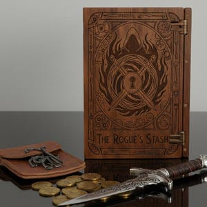 May include: A wooden box with the text "The Rogue's Stash" and an engraved design featuring a hooded figure, crossed swords, and a keyhole. A small leather pouch with keys, a dagger, and gold coins are in front of the box.