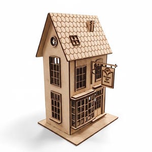 Pode incluir: Uma maqueta de casa em madeira clara, com telhado de telha, múltiplas janelas e um letreiro que diz "Hannah's Tea House". A casa em miniatura é construída sobre uma base retangular.