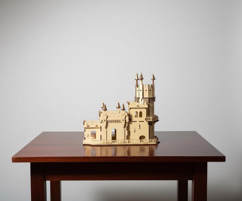 Pu&ograve; includere: Un modello in legno tagliato al laser di un castello dettagliato, con pi&ugrave; torri, finestre ad arco e intricati dettagli architettonici. Il modello &egrave; di colore beige chiaro e poggia su un tavolo di legno marrone scuro.