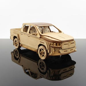 Puede incluir: Maqueta de madera de una camioneta pickup con detalles intrincados, incluyendo cabina, caja y ruedas. El modelo de madera clara se muestra sobre una superficie reflectante.