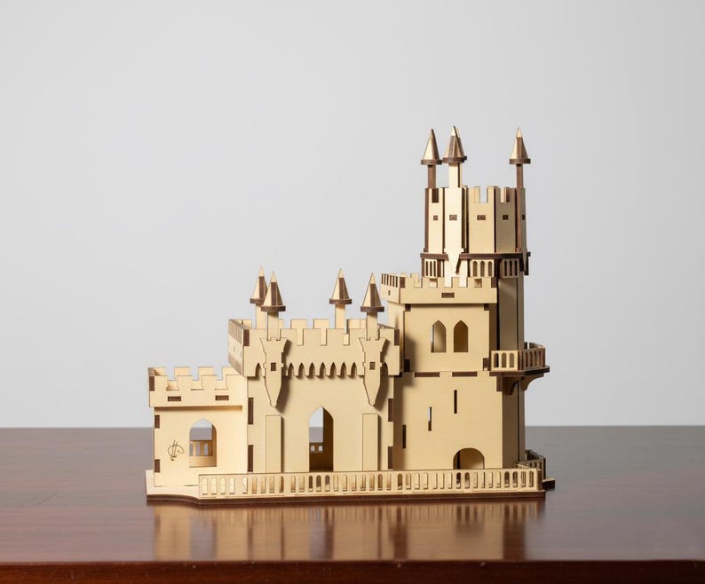 Pu&ograve; includere: Un modello di castello in legno con pi&ugrave; torri, merlature e porte ad arco. Il castello &egrave; costruito in legno chiaro con accenti pi&ugrave; scuri e poggia su una superficie di legno. Il modello ha un design dettagliato, che mostra una struttura architettonica in miniatura.
