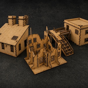 May include: Three miniature wooden building models. One is a complete building with a sloped roof and chimneys. Another is a partially destroyed building. The third is a square building with a flat roof and stairs.