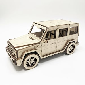 Może przedstawiać: Drewniany model samochodu sportowo-użytkowego (SUV) z precyzyjnymi detalami, w tym kołami, oknami i przednim grillem. Model wykonany jest z jasnego drewna i stoi na białej powierzchni. Model SUV to szczegółowa replika.