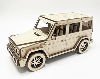 May include: A wooden model of a sport utility vehicle (SUV) with detailed features, including wheels, windows, and a front grille. The model is made of light-colored wood and sits on a white surface. The SUV model is a detailed replica.