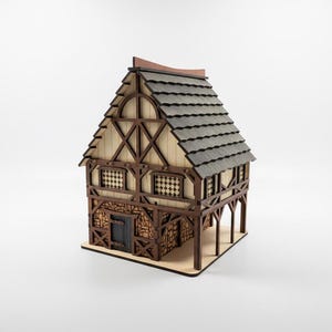 Peut inclure: Une maquette de bâtiment médiéval en bois avec un toit en pignon. La structure présente un toit en bardeaux gris foncé, des murs beige clair et des poutres en bois brun foncé. Le bâtiment a deux fenêtres avec des motifs décoratifs.