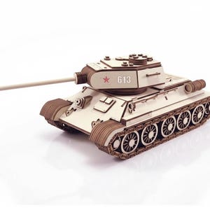 Pode incluir: Um modelo de madeira de um tanque, com um cano longo e rodas de esteira detalhadas. O tanque é principalmente bege claro com detalhes em marrom. A torre exibe o número "613" e uma estrela vermelha.