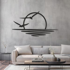 Puede incluir: Arte de pared de metal negro que representa una escena de puesta de sol con dos pájaros en vuelo. El sol es un círculo grande y el agua está representada por líneas onduladas. Esta pieza decorativa añade un toque de naturaleza a cualquier espacio habitable.