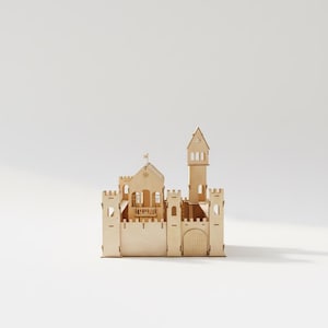 May include: A wooden castle model with a tall tower, arched doorway, and multiple turrets. The light-colored wood construction features detailed cutouts for windows and decorative elements. A small flag is atop the main building.