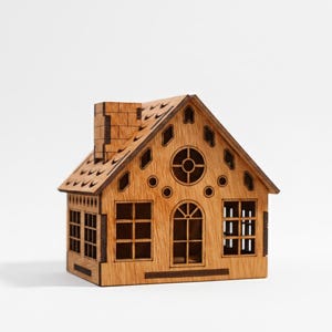 Puede incluir: Un adorno decorativo con forma de casa de madera con chimenea, ventanas y una ventana redonda. La casa está hecha de madera marrón claro y tiene un diseño de techo detallado. Las ventanas están recortadas, permitiendo el paso de la luz.
