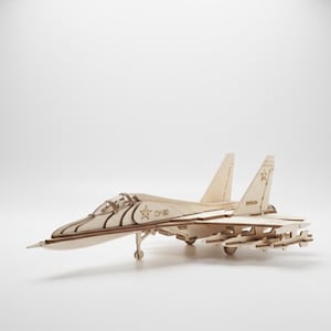 May include: A light-colored wooden model of a fighter jet, featuring detailed wings, tail fins, and a cockpit. The model includes visible weaponry and the text "CY-30" on the side. The toy is made of light-colored wood.
