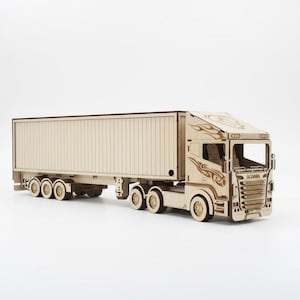 May include: A wooden model of a semi-truck and trailer. The truck has decorative flame designs and the word "SCANIA" on the front. The trailer has a ribbed design. The model is made of light-colored wood.