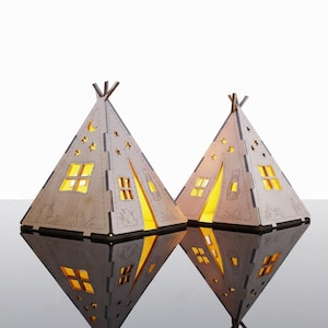Puede incluir: Dos lámparas de madera con forma de tipi con ventanas recortadas y formas de estrella. Las lámparas están iluminadas desde dentro, proyectando un brillo cálido. Las lámparas se reflejan en una superficie brillante. Adecuado para la decoración del hogar.