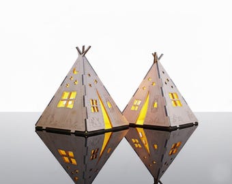 May include: Two wooden teepee-shaped lamps with cut-out windows and star shapes. The lamps are lit from within, casting a warm glow. The lamps are reflected on a glossy surface. These decorative lamps are suitable for home decor and measure approximately 20 cm in height.