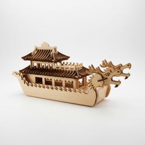 May include: A wooden dragon boat model with a detailed pagoda-style structure. The boat features a dragon head at the front and is crafted from light-colored wood with darker accents, showcasing intricate architectural details.