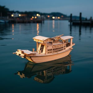 Op de afbeelding: Een houten modelboot drijft op het water en weerspiegelt zijn gedetailleerde ontwerp. De boot heeft een overdekte cabine, ingewikkelde gravures en een lichte houten afwerking. De achtergrond toont een vage waterkant met lichten.
