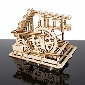 Könnte beinhalten: Ein hölzernes Murmelbahn-Set mit Zahnrädern, Rampen und Bahnen. Das Set besteht aus hellem Holz und weist ein komplexes Design mit mehreren Ebenen und beweglichen Teilen auf. Mehrere Metallmurmeln sind sichtbar.