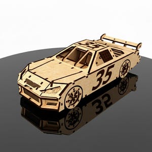 May include: A wooden race car model with the number 35 on the side and top. The car has a spoiler and detailed wheels. The model is made of light-colored wood and sits on a reflective surface.