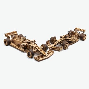 以下が含まれることがあります： 木製のF1レーシングカーモデル2台。車は、ホイール、スポイラー、スポンサーロゴなど、複雑なディテールを備えた明るい茶色の木材で作られています。1台の車には番号16、もう1台には「Oracle」の文字が書かれています。
