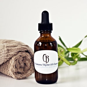 May include: A brown glass bottle with a dropper top and a white label that reads "CB Tamanu Thyme Oil Cleanser Cleansing Blend for Acne and Oily Skin".