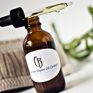 May include: A brown glass bottle with a dropper filled with a clear liquid. The bottle has a white label with the text "Camanu Thyme Oil Cleanser" and "Blending blend for Acneic and Oily skin".